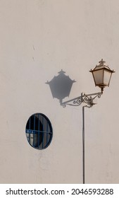 Street lamp and shadow with small round blue window on white wall