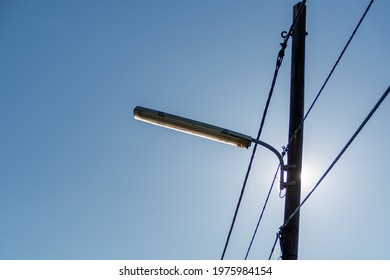 A street lamppost with wires. Wooden pole with a lantern and electric cables in silhouette against the sun.
