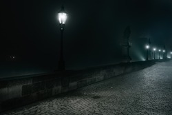 Street Lamps And Light From Them On The Old Stone Charles Bridge In The Night Fog And Silhouettes Of Figures