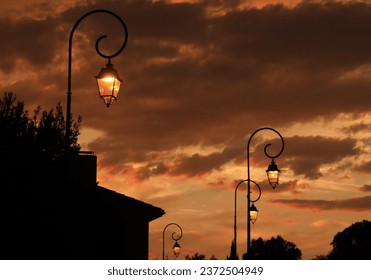 Street lanterns against backdrop of silhouetted buildings and cloudy skies at sunset in France - Powered by Shutterstock