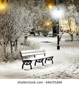 Street Light And A Bench. Snow On Trees In Riga Old Town Park By Night