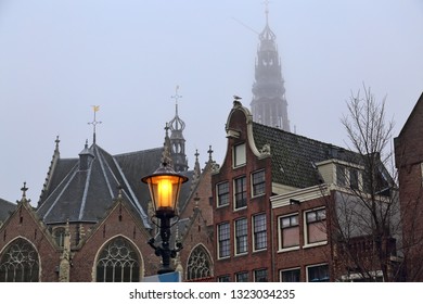 Street light and the Old Church with the tower sticking out above historical houses in foggy weather in Amsterdam, Holland