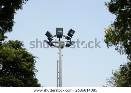 Street light pole with multiple flood lamps surrounded by tree branches under clear blue sky in Semarang Old Town, Central Java, Indonesia, on September 3, 2022.