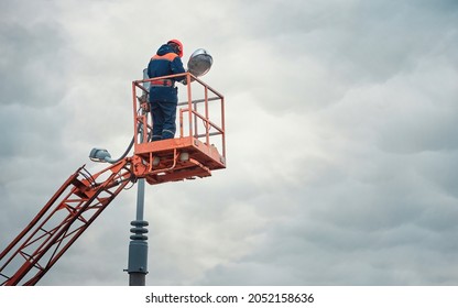 Street Light Repair Works, Worker Repair Street Lamp At Height, Led Lights Replacement. Man In Lift Bucket Wearing Personal Protective Equipment Fix Light Pole Lamp. 