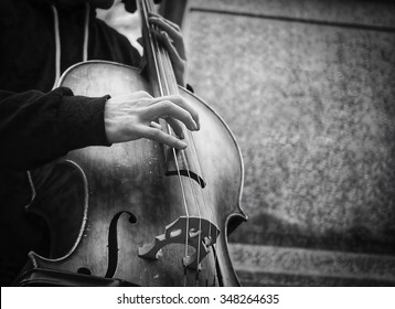 Street Musician's Hands Playing Bass On An Acoustic Instrument In Urban Environment In Winter.