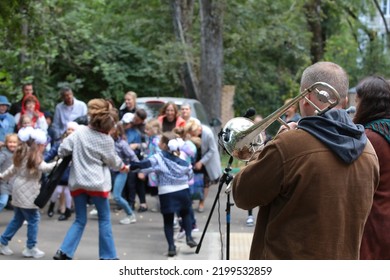 Street Musicians Performing Outdoors In The Park Play The Trombone And Sing In Front Of Happy Dancing Kids.Holiday Concept