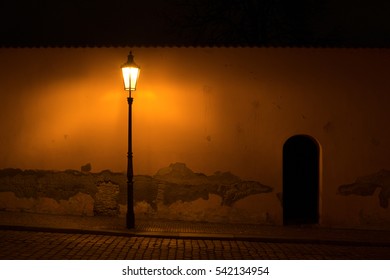 Street with old retro lamp post in front of the wall with cracked plaster. Dark scenery during night. Scene is lit by poor yellow light of lantern ( dark exposure ) - Powered by Shutterstock