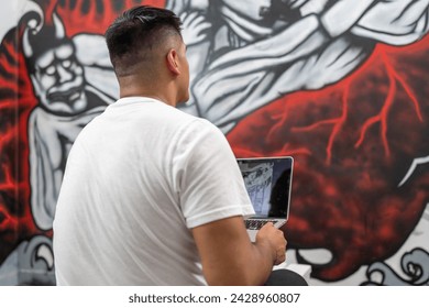 Street painter using a laptop to work on a new mural indoors - Powered by Shutterstock