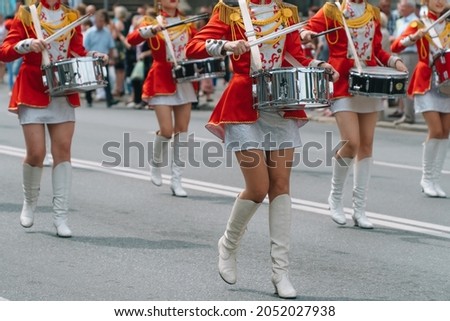 Street performance of festive march of drummers girls in red costumes on city street. Young girls drummer in red vintage uniform at the parade