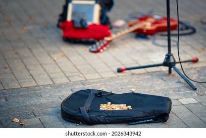 Street performers busking money. Street musician, guitar player make money. Guitar bag with coins and equipment of street musician in background. 