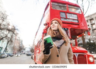 A Street Photo Of A Young Woman In A Coat And Cap Walking Down The Street With A Cup Of Coffee In Her Hand And Looking Away. Walk On A Cool Christmas Day. Winter Concept.