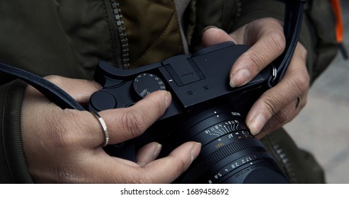 Street photographer adjusts settings on her manual camera changing the focus while shooting from the hip - Powered by Shutterstock