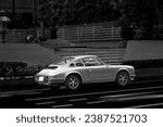 Street photography in Tokyo. A vintage sports car in front of a staircase of the park entrance. A black and white photo with vivid shades of grey creating a retro-vintage look and feel in this photo.