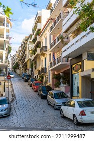 Street In Piraeus, Greece. Vertical View Of Parked Car, Buildings, Sky And City Road Up In Summer. Theme Of Mountain Town, Culture, Tourism And Travel. Athens - May 7, 2018