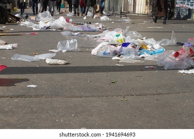 street pollution - trash and plastics flying on the city pavement with anonymous pedestrians walking through garbage in dirty, polluted streets