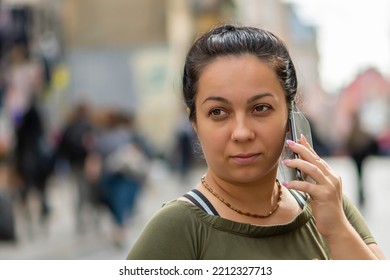 A Street Portrait Of A 35-40 Year Old Woman Talking On A Smartphone Against The Backdrop Of A Blurry Summer City And A Crowd Of People.