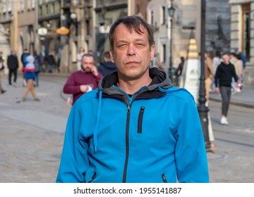 Street Portrait Of A 45-50-year-old Man With A Serious Expression On A Neutral Urban Background, Medium Plan. Maybe He's A Tourist Or A Retired Military Man, An Actor Or A Truck Driver.