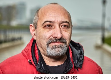 Street Portrait Of A Chubby Balding Man With A Gray Beard. Middle-aged Businessman Photographed Close-up In Cloudy Weather, Autumn Day.