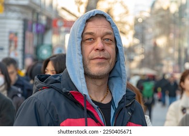 Street Portrait of an elderly man 45-50 years old on a blurry background of a street and a crowd of people in a European city.