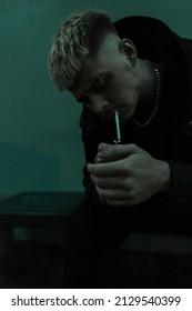 Street Portrait Of A Handsome Brutal Hipster Man With Hairstyle And Black Clothes Lighting A Cigarette And Smoking In The City At Night