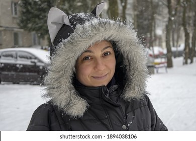 Street Portrait Of A Happy Woman 35-40 Years Old In Contact Lenses In Winter In A Jacket With A Fur Hood On The Street.