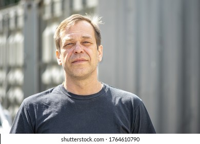 Street Portrait Of A Man 40-50 Years Old In A Black T-shirt On A Neutral Blurred Background. Perhaps He Is Just A Buyer, An Actor Or A Truck Driver, A Loader Or A Military Pensioner,