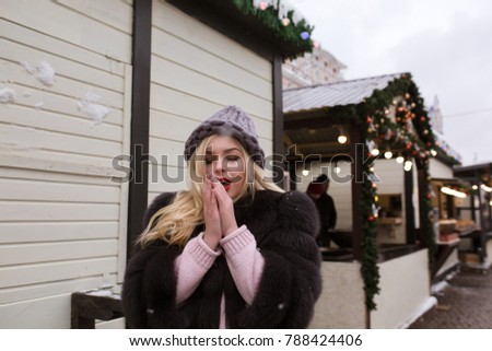 Street portrait of pretty blonde woman warm her hands at the Christmas fair. Space for text