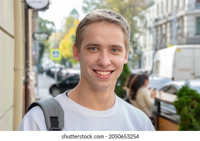 Street portrait of a smiling young guy 20-25 years old with a backpack on his shoulder against the background of old urban architecture. Perhaps he is an IT specialist or a tourist, a student 1.