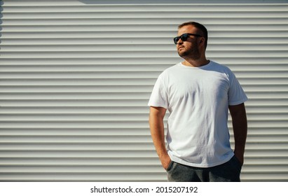 Street portrait of a young bearded man wearing white blank t-shirt standing on the street. Mock-up for print. T-shirt template.