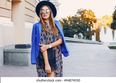 Street Portrait Of A Young Beautiful Elegant  Woman Holding Dark Leather Handbag. Lady Wearing Stylish  Spring Clothes, Trendy Hat And Sunglasses. 