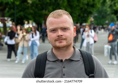 Street Portrait Of A Young Man With A Short Haircut In The City Center Against The Background Of People Passing By.