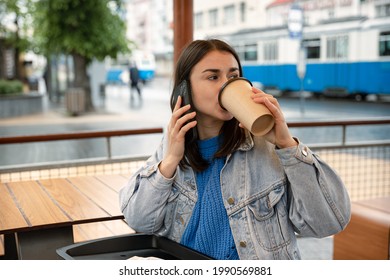 Street Portrait Of A Young Woman Who Is Drinking Coffee, Talking On The Phone And Waiting For Someone.