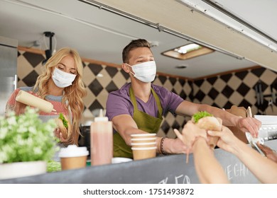 street sale and people concept - young sellers wearing face protective medical mask for protection from virus disease serving customers at food truck - Powered by Shutterstock