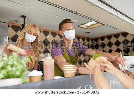 street sale and people concept - young sellers wearing face protective medical mask for protection from virus disease serving customers at food truck