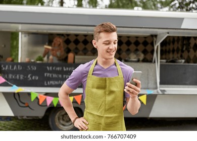 street sale, technology and people concept - happy young salesman in apron with smartphone at food truck - Powered by Shutterstock