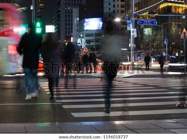 Street Scene with People Crossing the Street at Night.
Crowd of Busy People Walking in Major City. Buses and Cars Passing.
Cold Weather at Night. City Street with Skyscraper Buildings and
Lights.  
