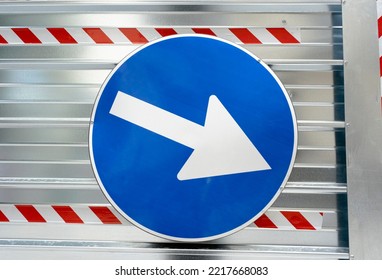A street sign, a white arrow over a blue circle, screwed up over the sheet metal protecting a construction site. Daylight closeup shot.
