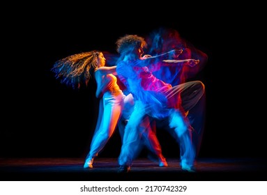 Street style dance. Young man and woman dancing hip-hop, breakdance isolated on dark background at dance hall in mixed neon light. Youth culture, hip-hop, movement, style and fashion, action.