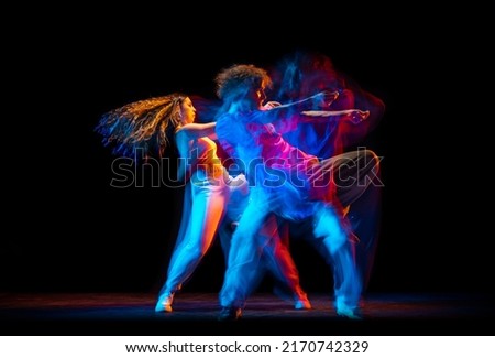 Street style dance. Young man and woman dancing hip-hop, breakdance isolated on dark background at dance hall in mixed neon light. Youth culture, hip-hop, movement, style and fashion, action.
