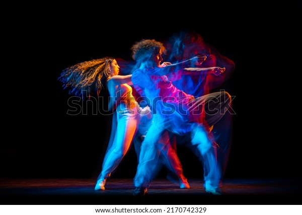 Street style dance. Young man and woman dancing\
hip-hop, breakdance isolated on dark background at dance hall in\
mixed neon light. Youth culture, hip-hop, movement, style and\
fashion, action.