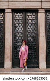 Street Style, Fashion Conception: Elegant Woman Wearing Trendy Pink Suit, Burgundy Color Hat, Zebra Print Sneakers,  Holding Yellow Bag, Walking In Street Of City. Full-length Outdoor Portrait