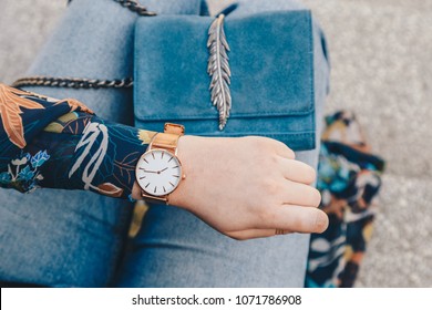 street style fashion details. close up, young fashion blogger wearing a floral jacker, and a white and golden analog wrist watch. checking the time, holding a beautiful suede leather purse.
