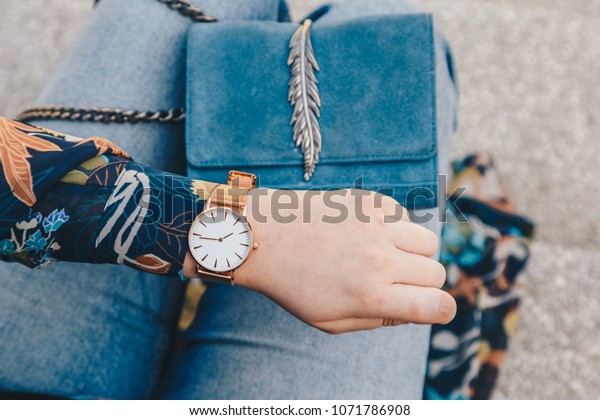 street style fashion details. close up, young\
fashion blogger wearing a floral jacker, and a white and golden\
analog wrist watch. checking the time, holding a beautiful suede\
leather purse.\
