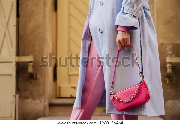 Street style, fashion details: small pink faux\
patent leather baguette bag in trendy outfit. Woman holding mini\
handbag. Copy, empty space for\
text