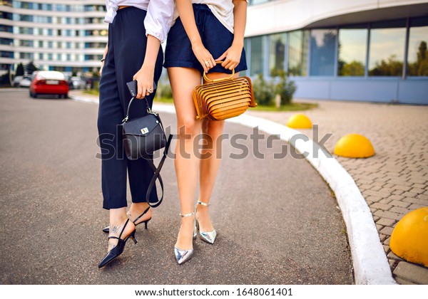 Street style\
fashion details of two women wearing elegant feminine classic\
outfits , kitten heel trendy shoes and luxury bags, focus on sexy\
long legs, spring summer hot vacation\
time.