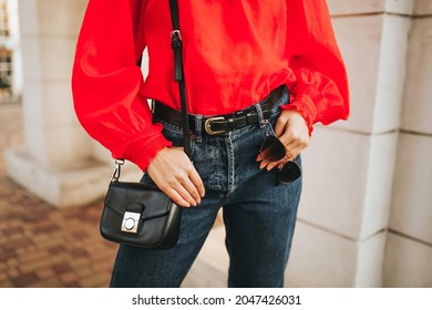 Street Style Fashion Details,  Woman Wearing Vintage Red Shirt, Blue Jeans, Black  Leather Bag And Clear Beige Sunglasses, Modern Classic Spring Autumn Chic Outfit, Warm Colours.