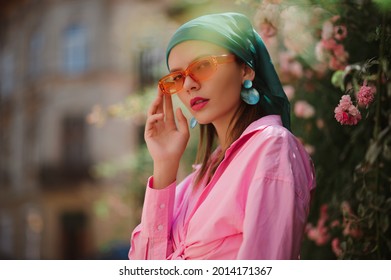 Street style fashion portrait of elegant woman  wearing trendy orange frame sunglasses, big green seashell earrings, trendy bandana, pink shirt, posing outdoor. Copy, empty space for text - Powered by Shutterstock