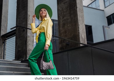 Street style, fashion portrait of happy smiling fashionable woman wearing green hat, wide leg jeans, yellow shirt, holding trendy zebra print, walking in city. Copy, empty space for text