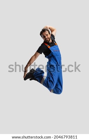 Street style.. Funny bearded young man, male auto mechanic in dungarees jumping isolated over white studio background. Concept of labor, occupation, funny meme emotions, ad. Looks stressed, worried