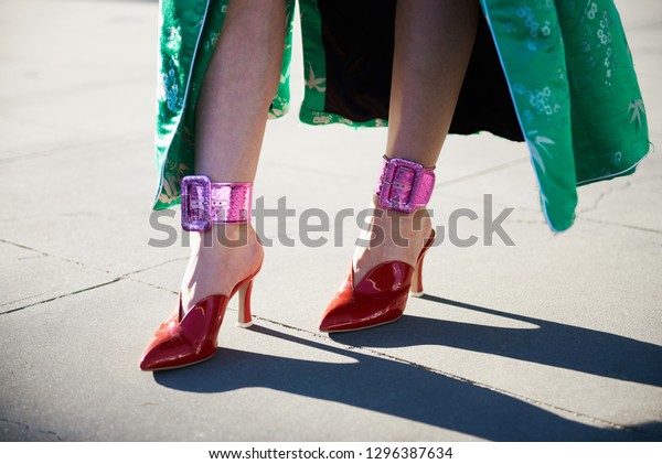 Street style image of stylish woman wearing\
pink metallic ankle cuffs, red mules and a green Chinese inspired\
jacket, horizontal